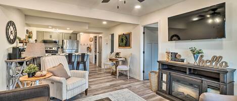 A spacious living room with a fireplace, a ceiling fan, and a television mounted on the wall.