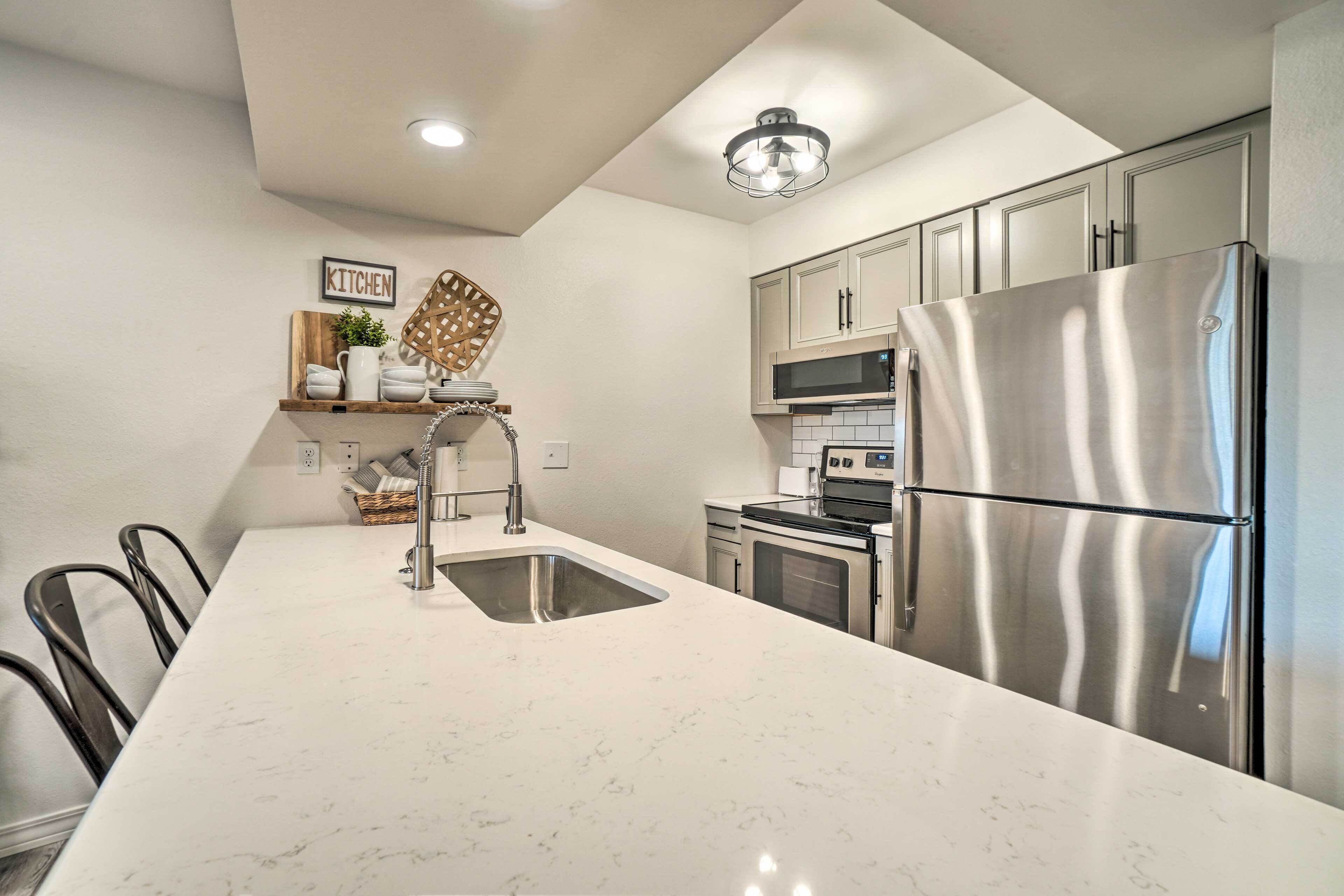 A modern kitchen with a stainless steel refrigerator, a microwave, and a sink. There is a wooden shelf with kitchenware and a sign that says "KITCHEN".