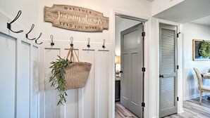 Un pasillo con un letrero de madera que dice “Que tu viaje siempre te lleve a casa”, una cesta tejida con follaje y una puerta con diseño persiana.