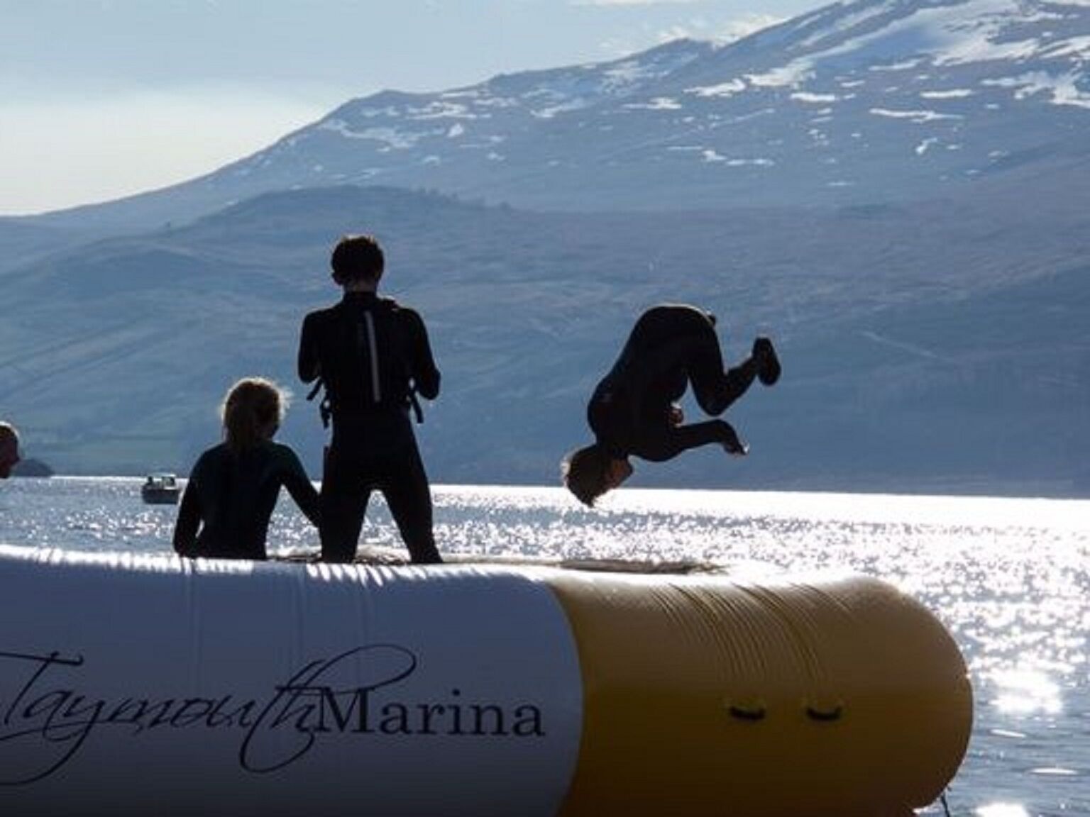 A person jumping off a large inflatable tube with a snowy mountain in the background.