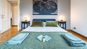 Una cama bien hecha con una manta verde, dos almohadas y un mapa mundial en la pared de arriba.