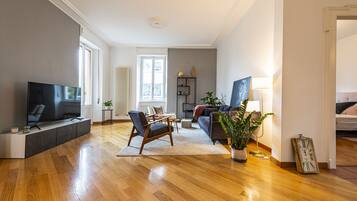 Een moderne woonkamer met een flatscreen televisie, een bank, een fauteuil en een potplant.