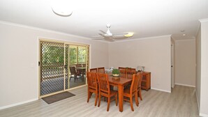 Ein Esszimmer mit Holztisch und -stühlen, einem Deckenventilator und einer Glastür zum Patio.