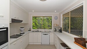 Eine moderne Küche mit weißen Schränken, einem eingebauten Backofen, einer Kaffeemaschine, einem Geschirrspüler und einem Fenster mit Blick ins Grüne.