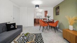 A modern living room with a grey sofa, a coffee table, and a dining area with orange chairs.