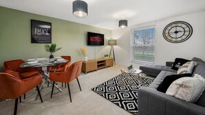 A modern living room with a dining area, a grey sofa, a black and white rug, and a wall-mounted clock.