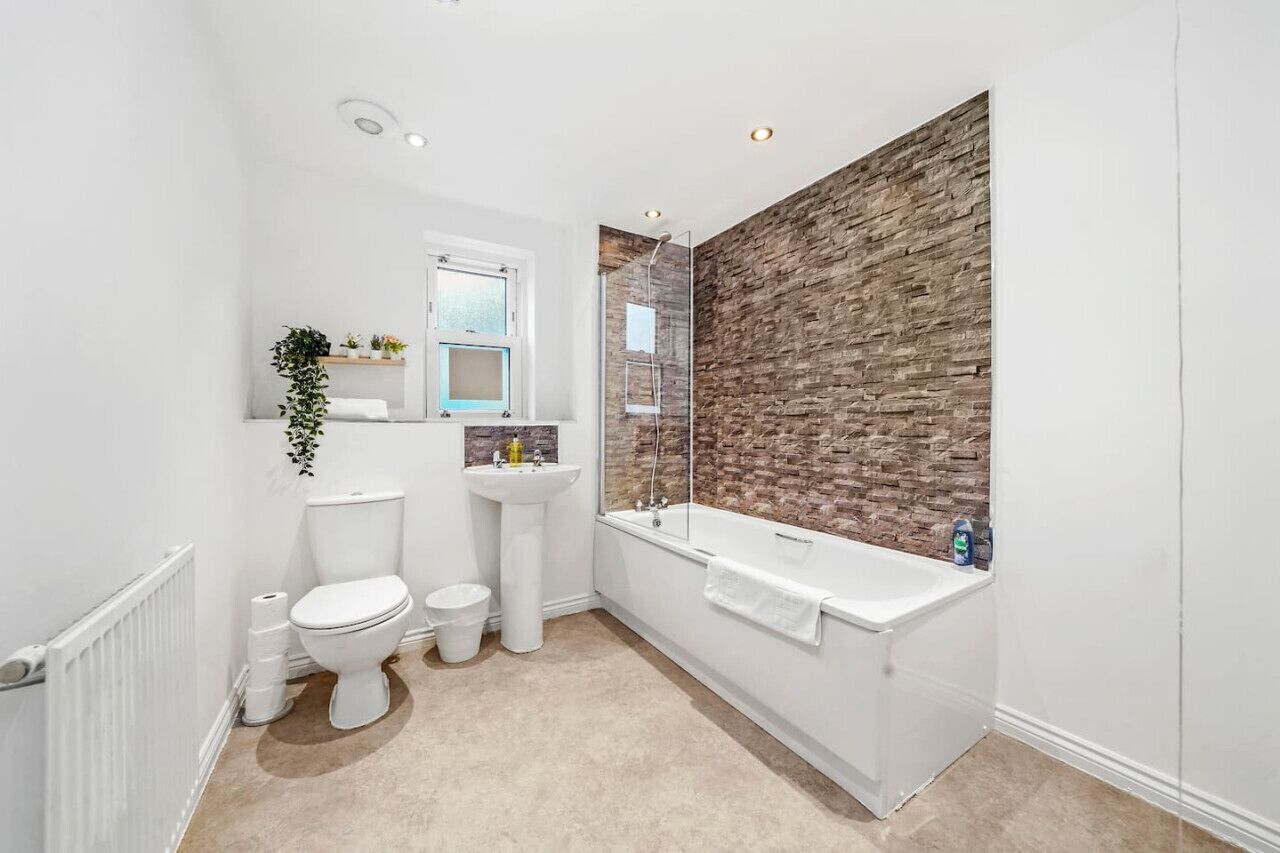 A modern bathroom with a white toilet, pedestal sink, and a freestanding bathtub.