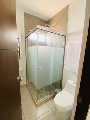 Ein Badezimmer mit einer gläsernen Dusche, einer Toilette und einem Handtuch an der Wand.