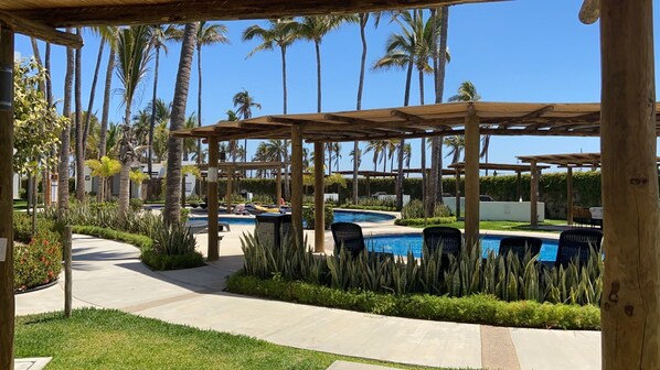 Ein Resort-Poolbereich mit mehreren Pools, überdachten Sitzbereichen und Palmen.