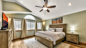 Quarto com cama, mesas de cabeceira, ventilador de teto e uma janela grande com cortinas.