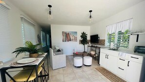 Et moderne køkken med hvide skabe, et spiseområde med bord og stole, samt en opholdsstue med sofa og fjernsyn.