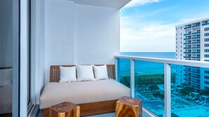 Un balcón con una cama, taburetes de madera y vistas al océano y edificios.