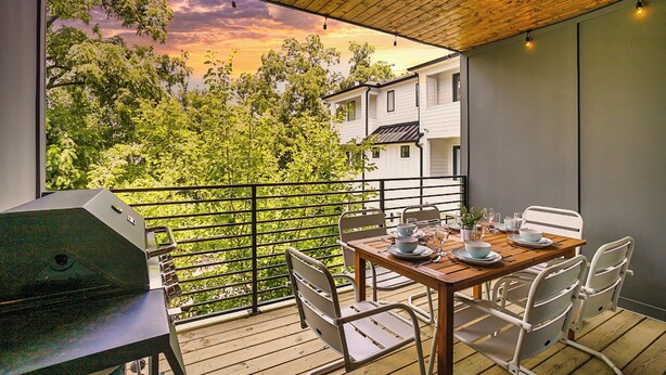 Ein Balkon mit Esstisch und Stühlen, der auf eine üppige grüne Landschaft und ein Gebäude im Hintergrund blickt.