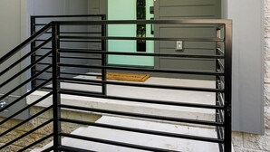 Eine Treppe mit schwarzen Geländern, die zu einer Tür mit grünem Türrahmen führt.