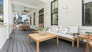 Een overdekt terras met een houten tafel, een bank en stoelen.