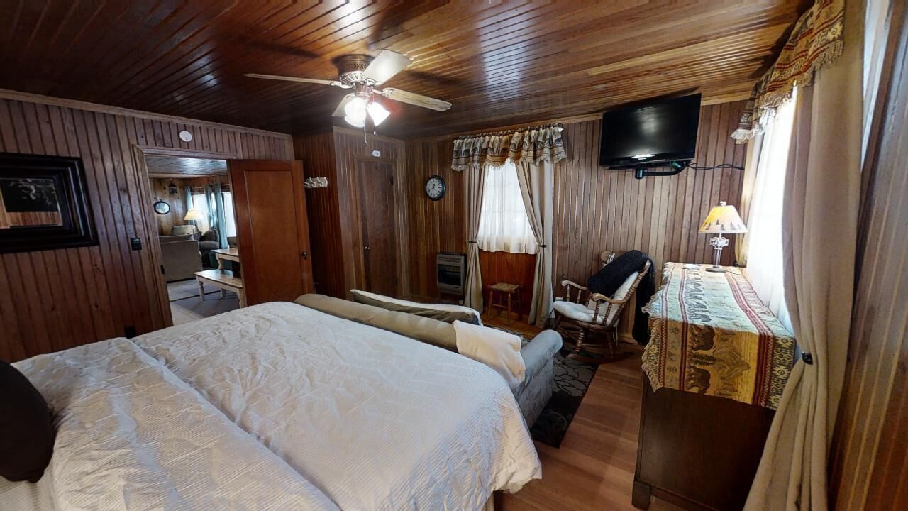 A wooden-paneled room with a large bed, a desk with a lamp, a television, and a clock on the wall.