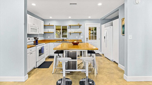 Una cocina moderna con armarios blancos, encimera de madera y una isla central con taburetes.