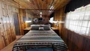 Una habitación de cabaña de madera con una cama grande, dos mesitas de noche y un ventanal con cortinas traslúcidas.