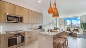 A modern kitchen with wooden cabinets, stainless steel appliances, and a central island with bar stools. - One Bedroom Condo King Bed With City Views (Miami)