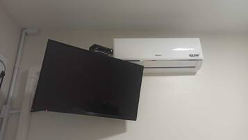 A white air conditioning unit mounted on a wall with a black object, possibly a TV, below it.
