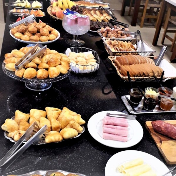 A buffet table with various food items including pastries, sandwiches, and fruits.