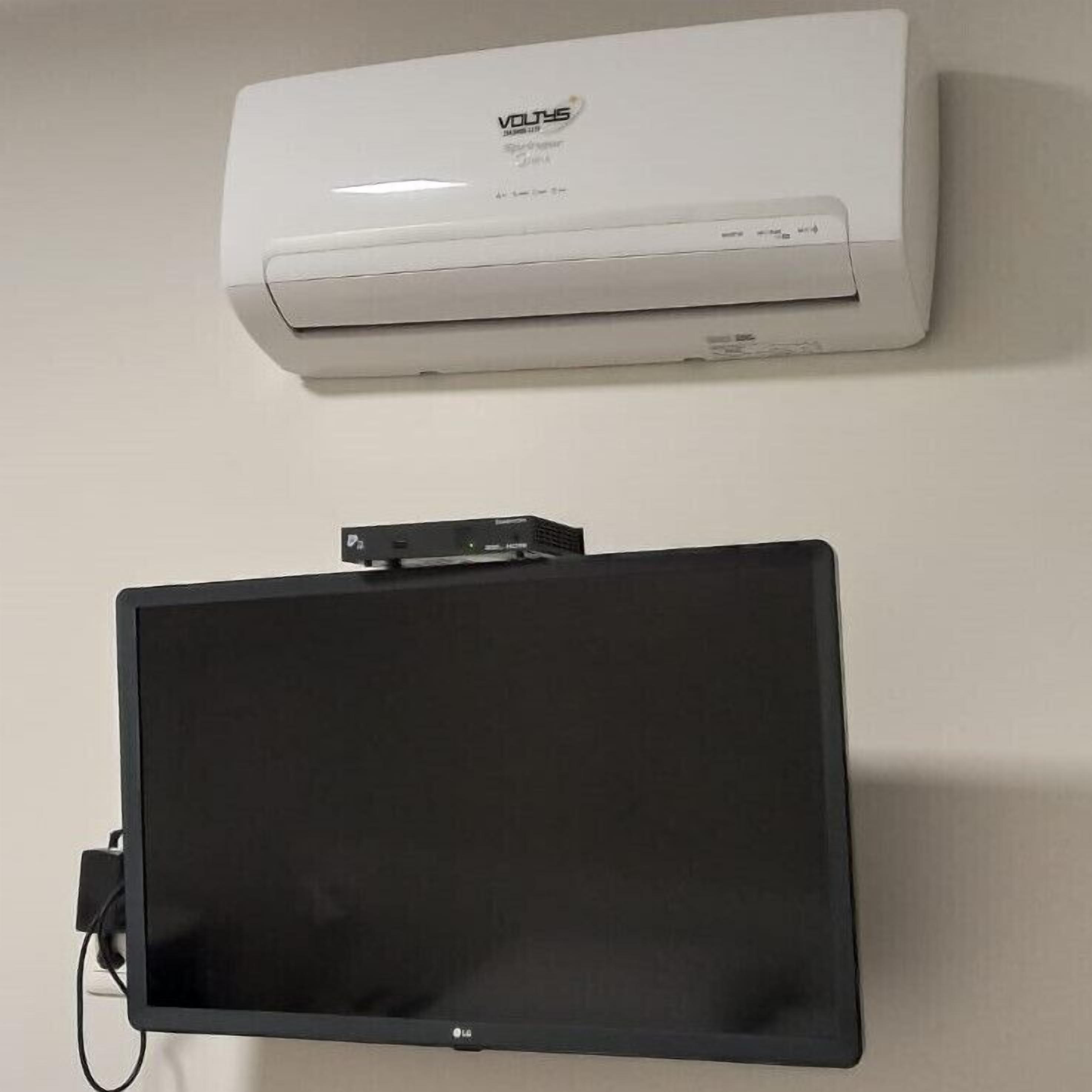 A white air conditioner and a black flat-screen TV mounted on a wall.
