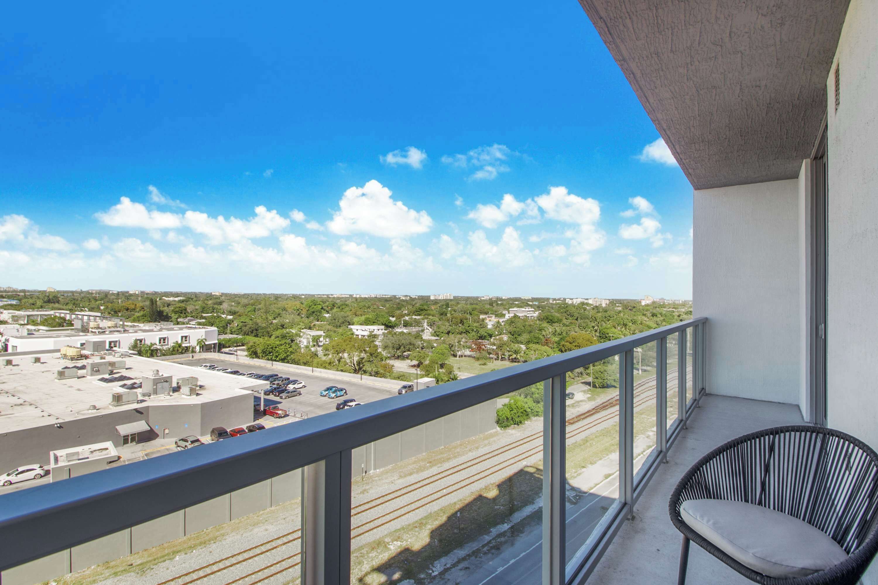 A balcony with a view of a parking lot, buildings, and a railway track.