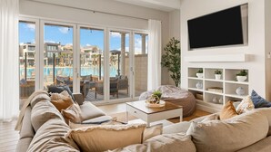 A living room with a sofa, a coffee table, and a TV mounted on the wall. - Persian Palms: Desert Color Lagoon + Beaches (St George)