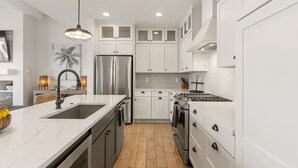 A modern kitchen with white cabinetry, stainless steel appliances, a marble countertop, and a wooden floor. - Persian Palms: Desert Color Lagoon + Beaches (St George)