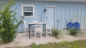 A house with a blue exterior, a white door, a window, and a small patio area with a table and chairs.