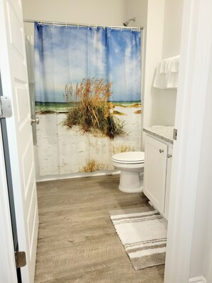A bathroom with a beach-themed shower curtain, a toilet, and a wooden floor.