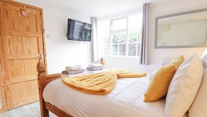 Ein Schlafzimmer mit einem hölzernen Bett, einem an der Wand befestigten Fernseher, einem Fenster mit Vorhängen und einem Holzschrank.