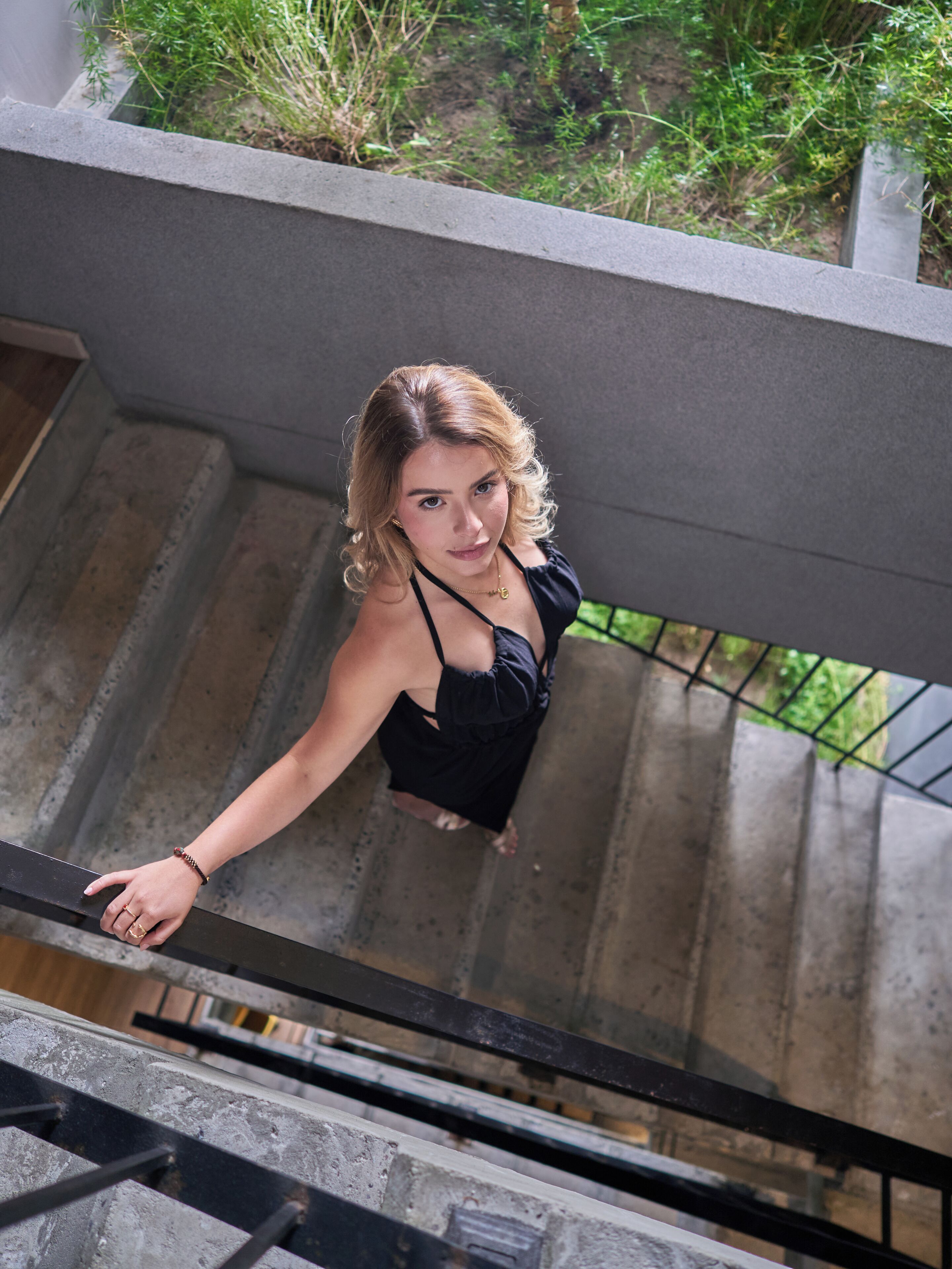 A person descending a concrete staircase with metal railings, surrounded by greenery.