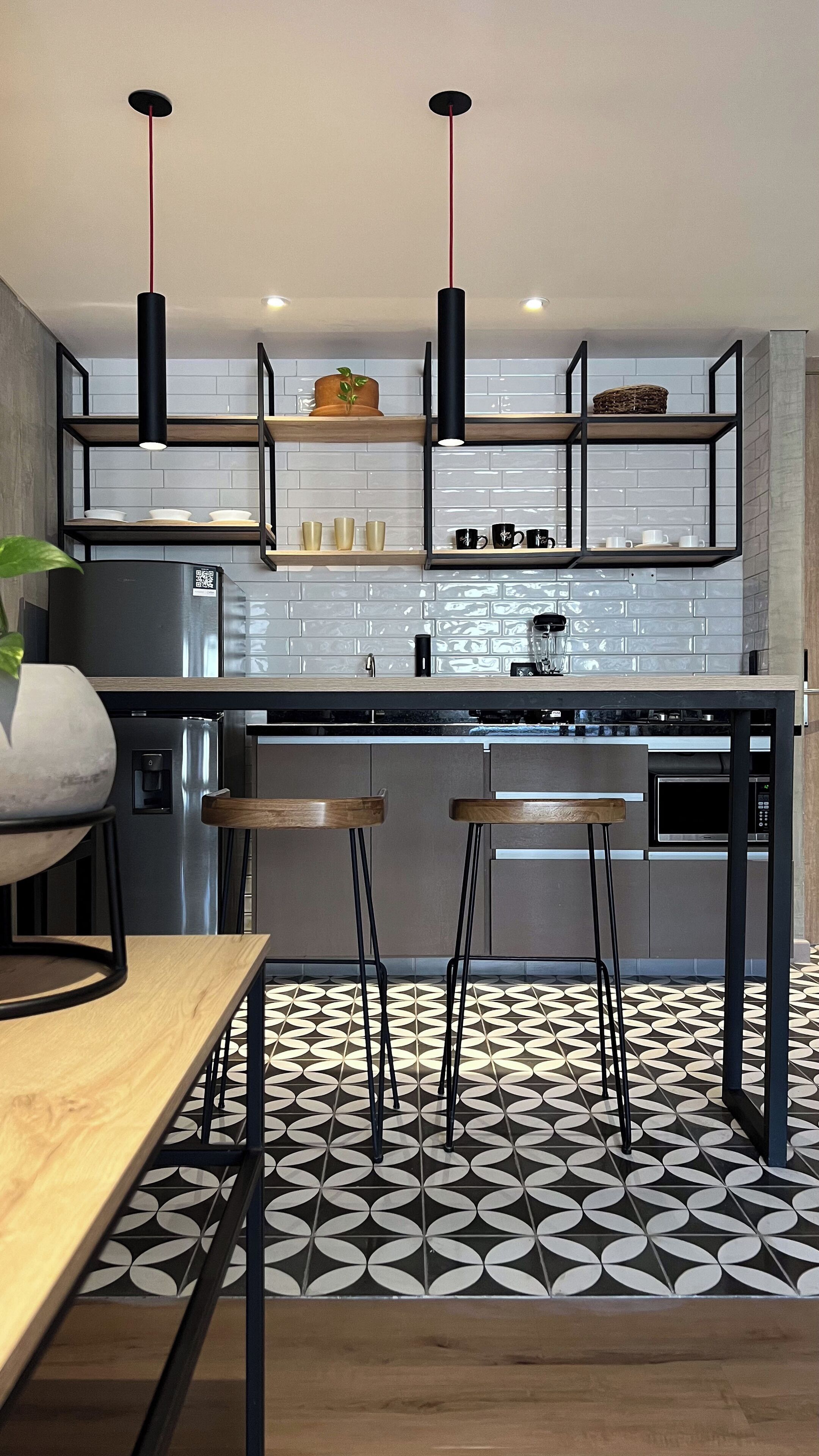 A modern kitchen with a central island, black pendant lights, and a patterned floor.