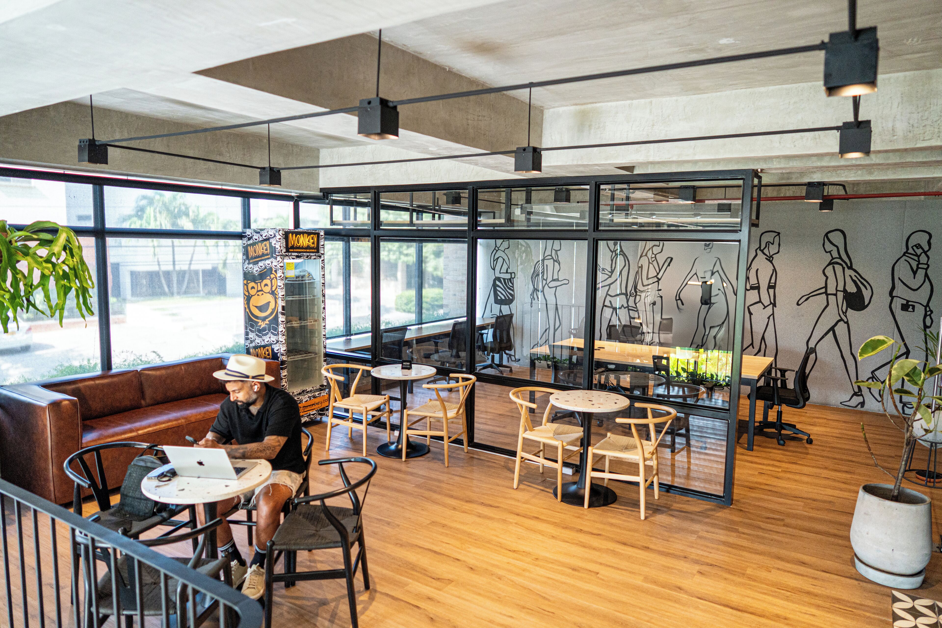 A modern cafe with wooden flooring, black and white chairs, and large windows.