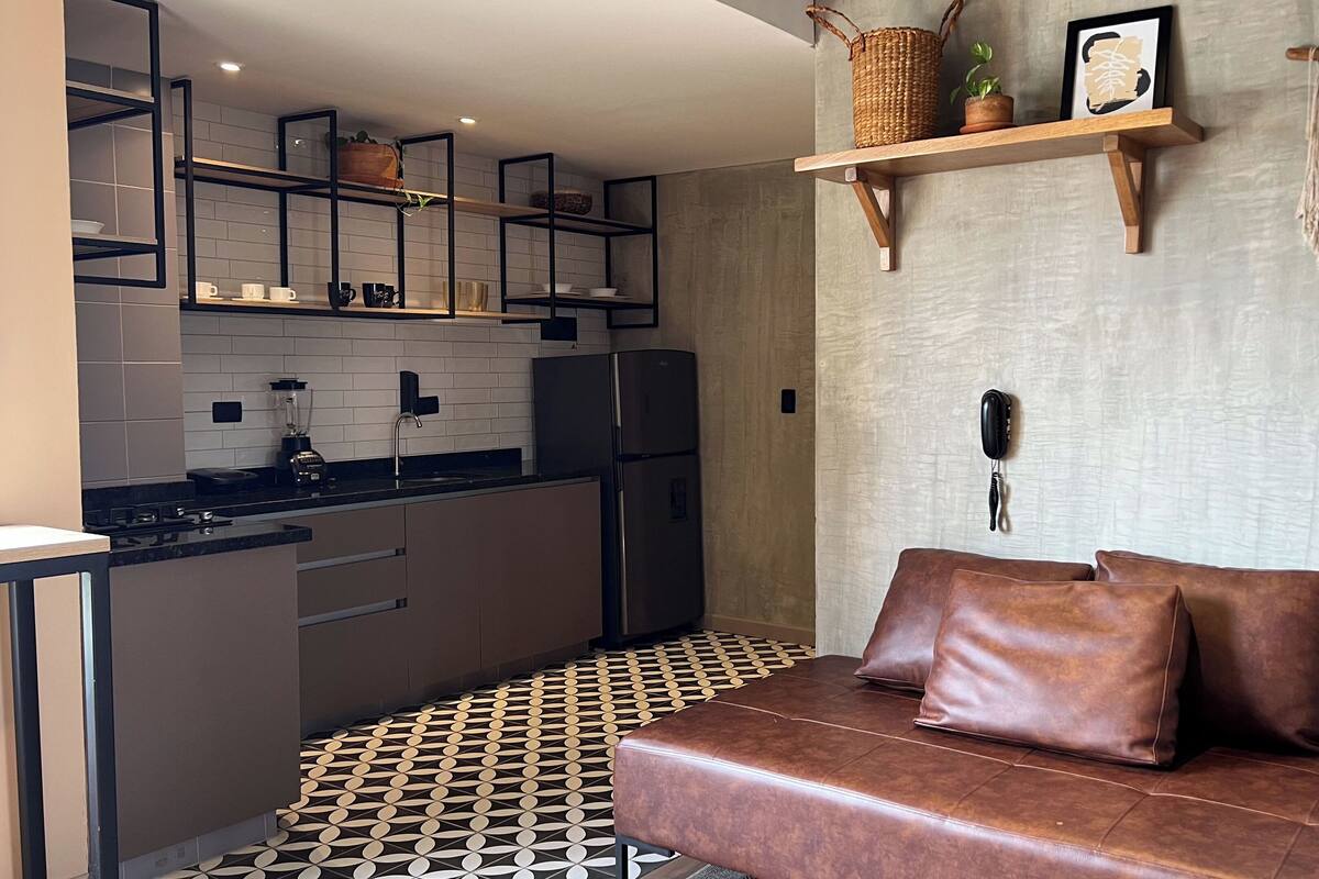 A compact kitchen with modern appliances, a dining area with a patterned floor, and a seating area with a leather couch.
