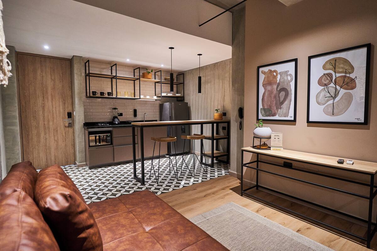 A modern kitchen with a wooden countertop, a built-in oven, and a refrigerator. There are stools and a bench in the dining area.