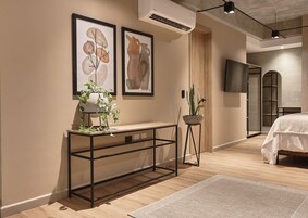 A modern bedroom with a bed, a console table with plants, a TV, and artwork on the wall.