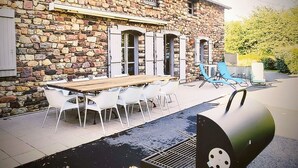 Un edificio de piedra con una terraza de madera, asientos exteriores y una parrilla.