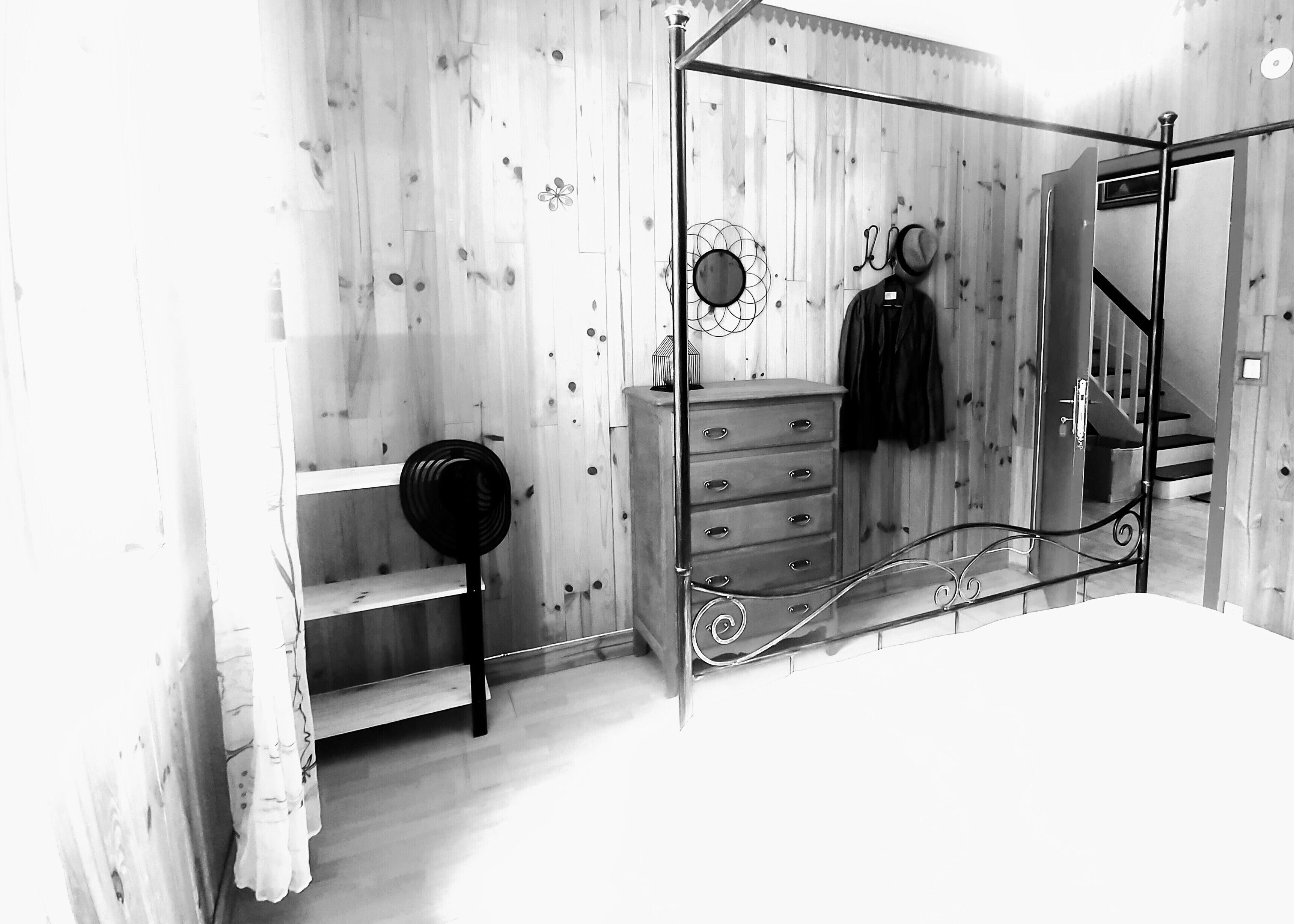 A bedroom with a wooden floor, a metal bed frame, a dresser with drawers, a mirror, and a hanging coat rack.