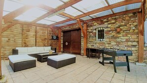 Un espacio al aire libre cubierto con vigas de madera, paredes de piedra, una puerta de madera, una mesa de fútbol de mesa y un sofá.