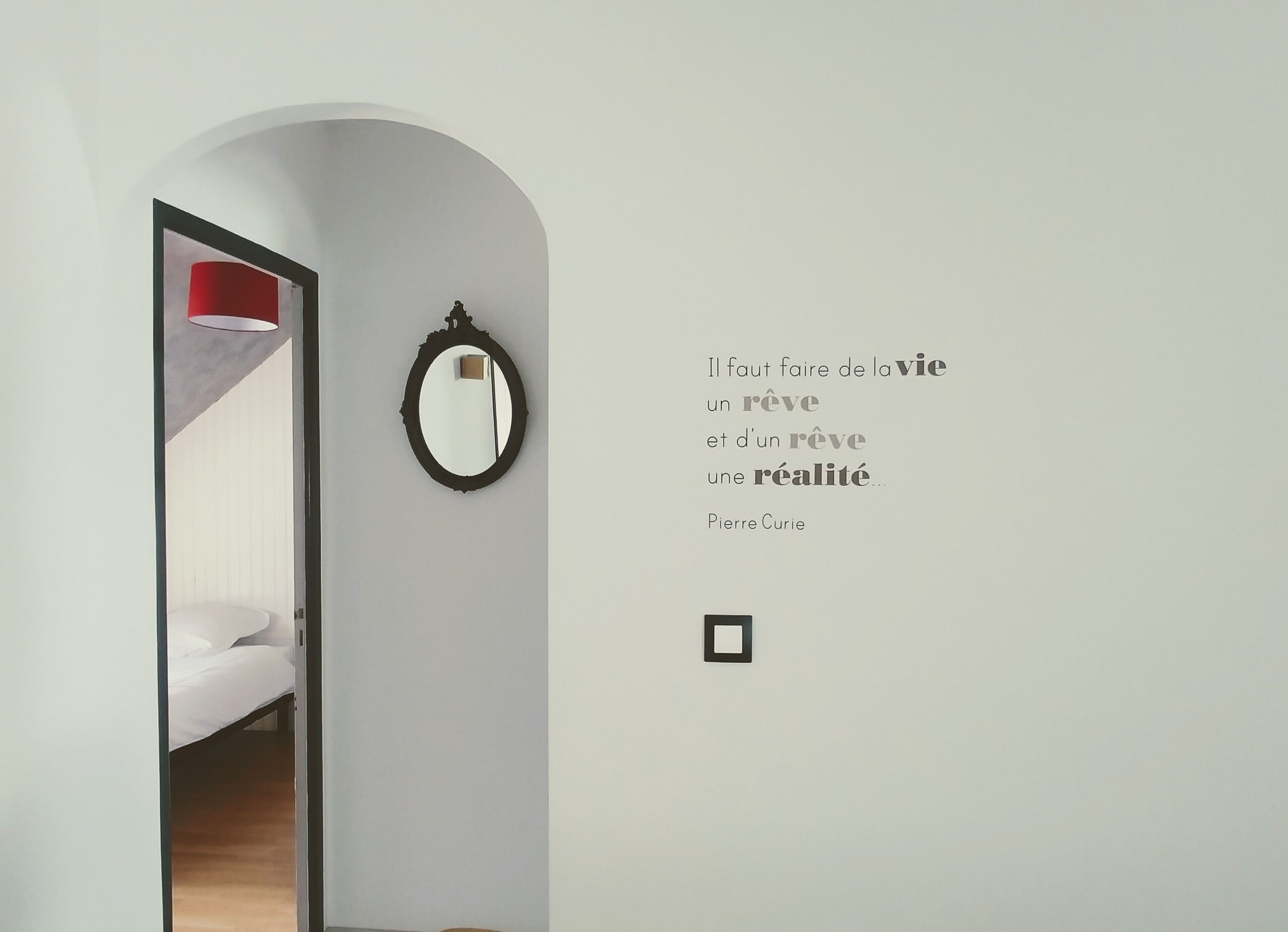 Ein schlicht eingerichteter Raum mit einem Bett, einem Spiegel und einer Wand mit einem Zitat.