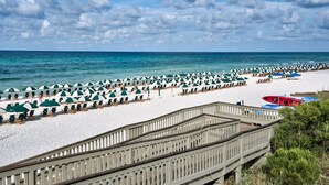 A beach with rows of umbrellas and chairs, a wooden walkway, and a view of the sea. - Rosemary Beach Penthouse | Southside of 30A with Gulf Views | Bikes Included (Rosemary Beach)