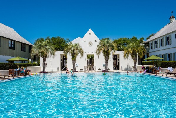 A swimming pool with palm trees, a building with a clock, and a clear blue sky.