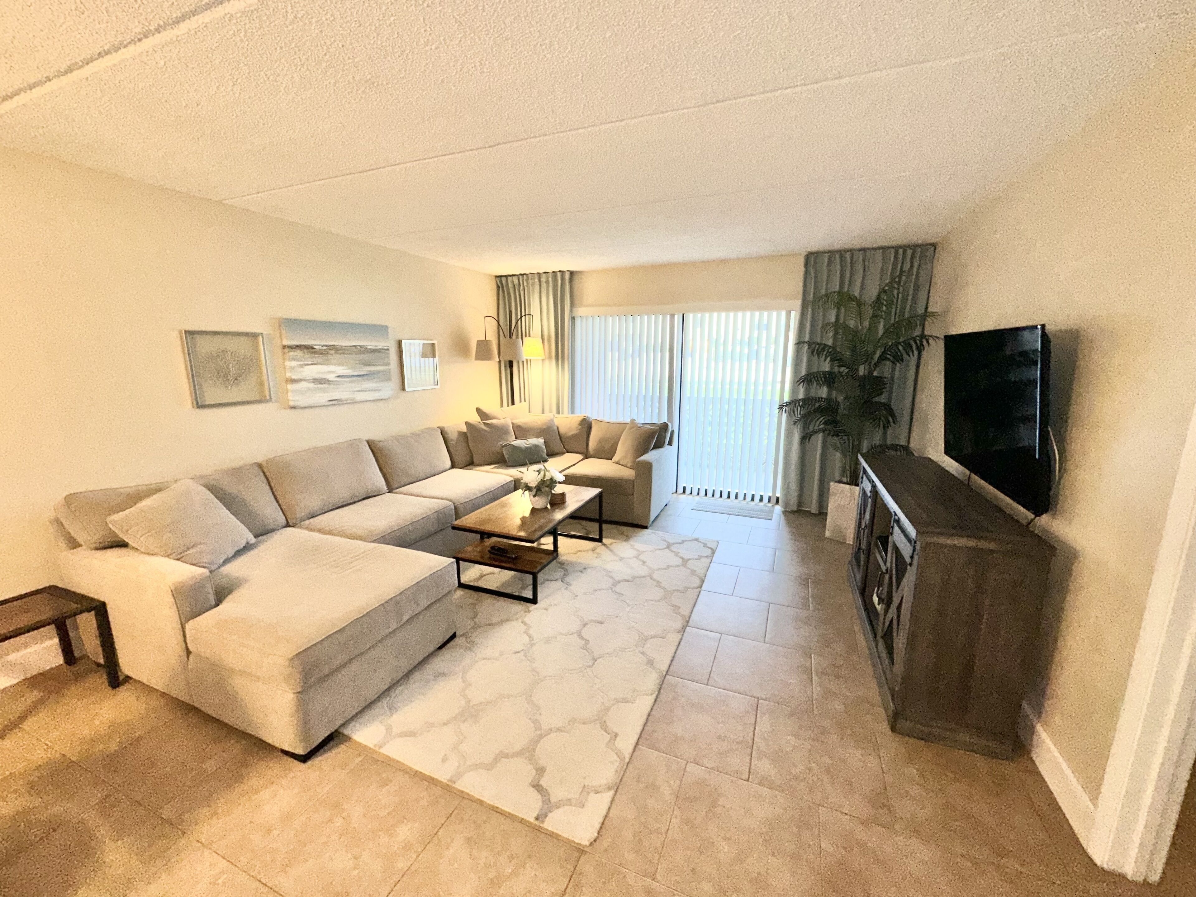 A modern living room with a sectional sofa, a coffee table, and a flat-screen TV mounted on the wall.