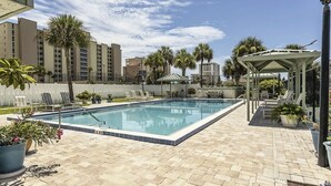 A rectangular pool with a tiled edge, surrounded by a paved patio with lounge chairs and potted plants. - Gorgeous Condo Steps From the Beach! (Daytona Beach Shores)
