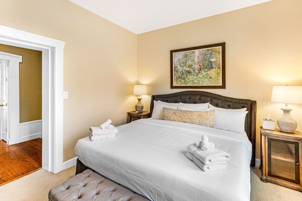 A hotel room with a large bed, two bedside tables with lamps, a painting on the wall, and a door leading to another room. - Perfect Getaway Walking Distance to Everything w/ Parking by Lucky Savannah (Savannah)