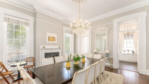 A dining room with a large table, white chairs, a chandelier, and a fireplace. - Exquisite Historic Mansion on Beautiful Pulaski Square by Lucky Savannah (Savannah)