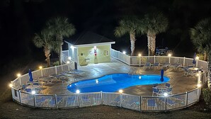 Ein Swimmingpool mit weißer Liegefläche und Liegestühlen, umgeben von einem weißen Zaun und Palmen.