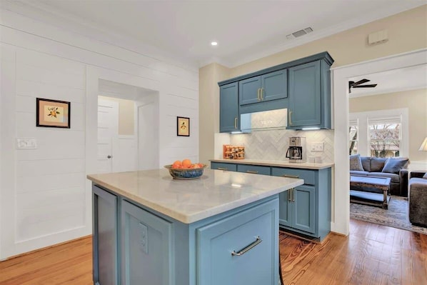 A kitchen with blue cabinets, a marble countertop, and a bowl of fruit.